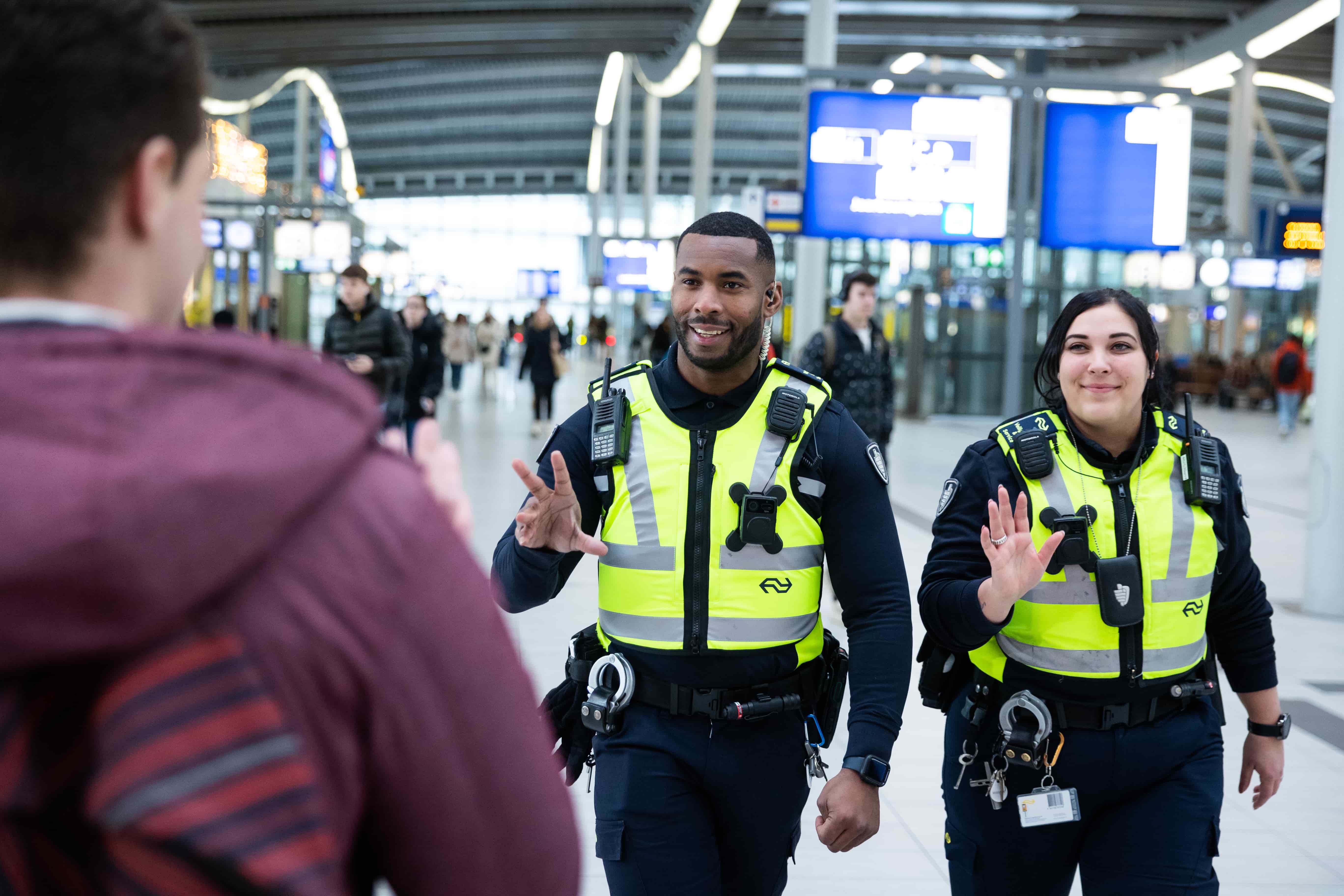 Op deze foto is NS-medewerker Veiligheid en Service Jaisal te zien in uniform op station Utrecht Centraal. Hij zwaait naar een reiziger.