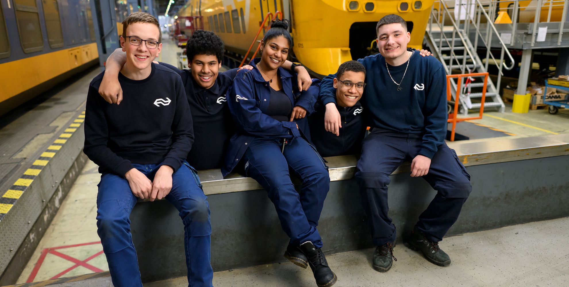 5 leerlingen van de monteursopleiding zitte lachend voor een stilstaande trein.